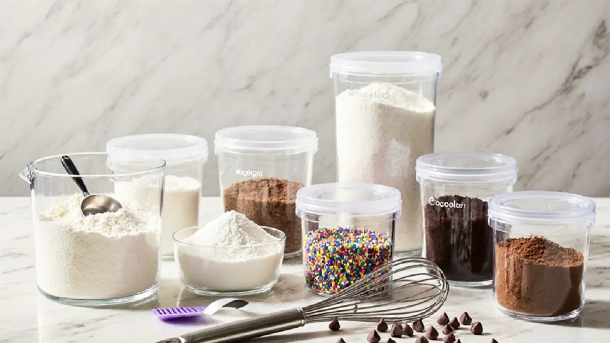 تصویر ظروف پلاستیکی در بسته مختلف روی کانتر آشپزخانه که مواد اولیه قنادی مانند کاکائو و شکر در آنها نگهداری میشود